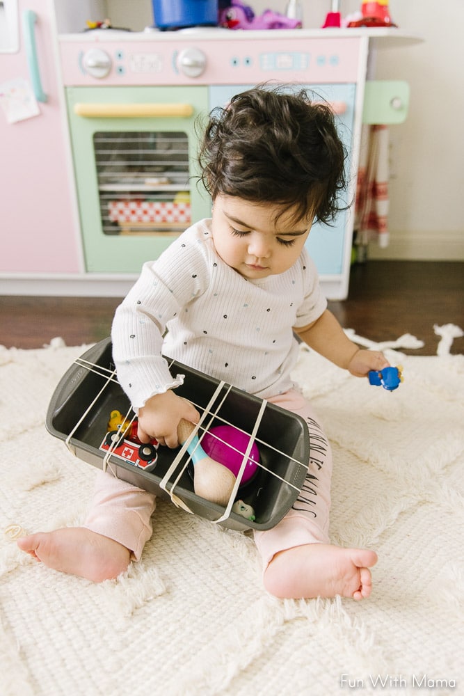 toddler playing with toys in a pan held in place by rubber bands 