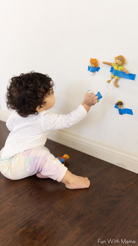 toddler sitting pulling tapes toys off the wall 