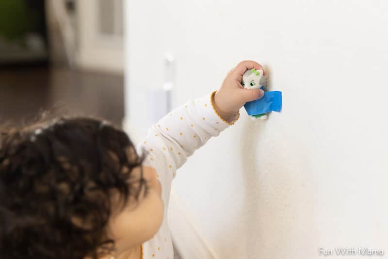 toddler pulling taped toy off wall 