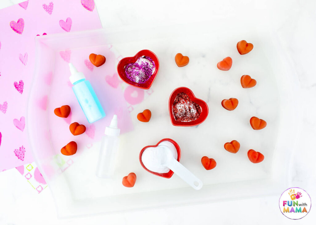 Setting up a science tray with ingredients including heart bowls, frozen baking soda hearts, vinegar, and baking soda powder