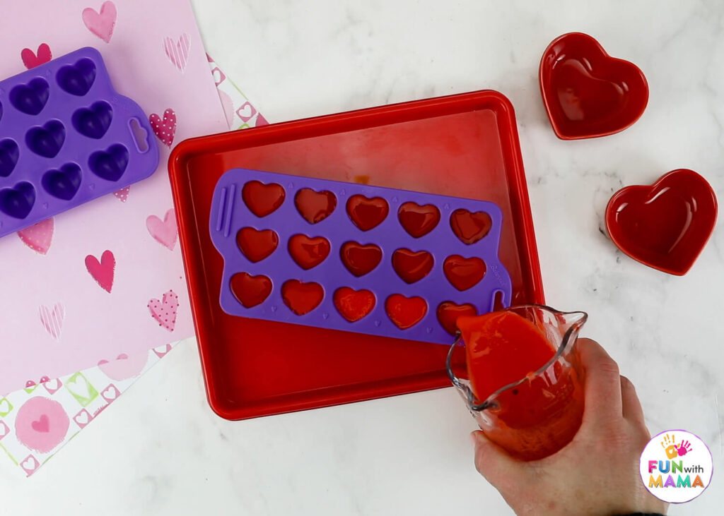 Pouring red baking soda mixture into heart ice trays